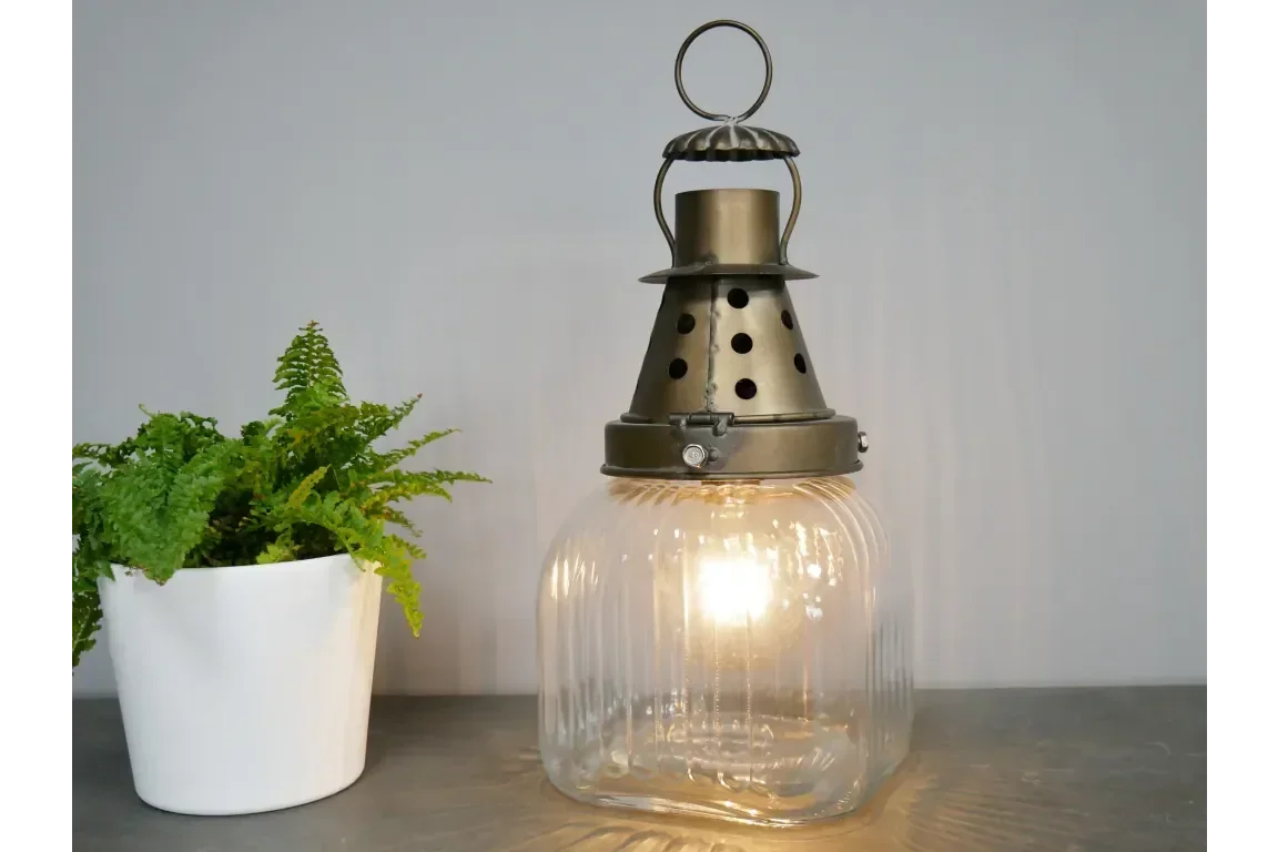Vintage glass lantern table lamp with metal top next to potted fern on grey surface