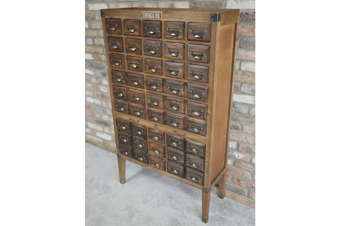 Tall vintage wooden storage cabinet with multiple drawers and metal handles against brick wall