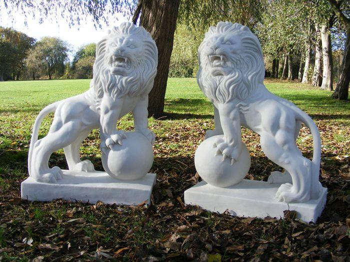 Pair of white stone lion statues with paws on spheres in park setting