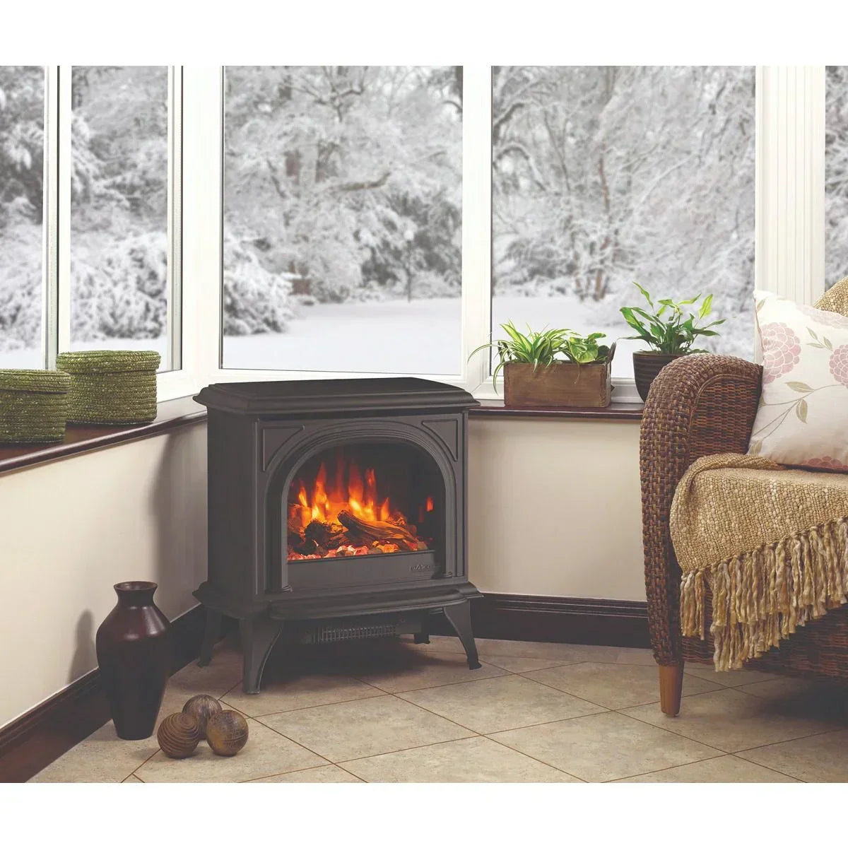 Electric stove heater in corner living room with wicker chair, plants, and snowy window view