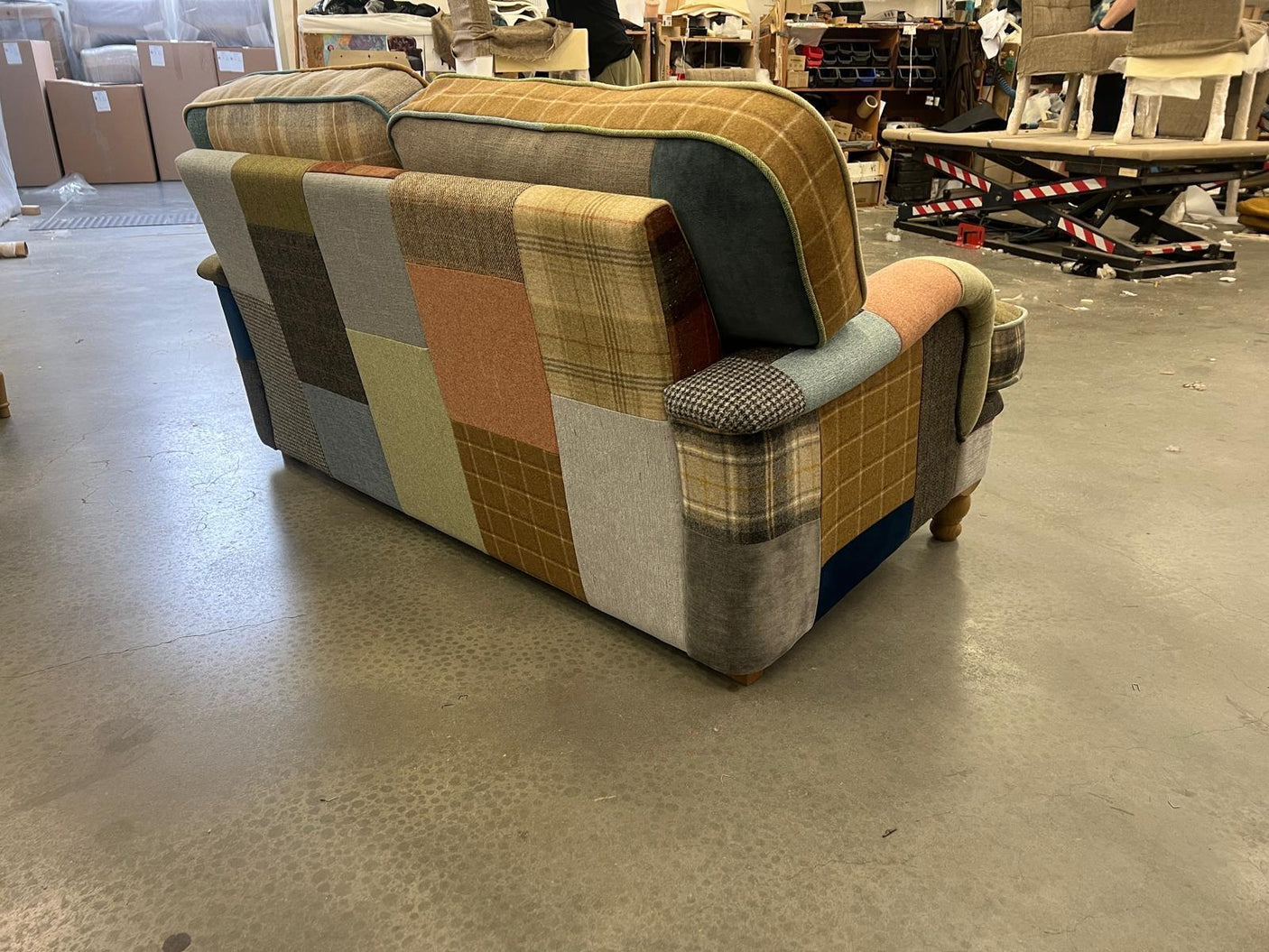 Patchwork fabric sofa with mixed plaid and solid panels, wooden legs, rear view in workshop
