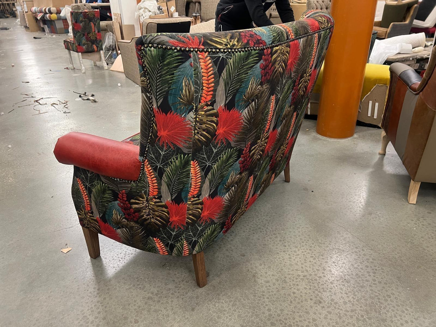 Floral accent chair with bold red armrest and dark wooden legs in a workshop setting