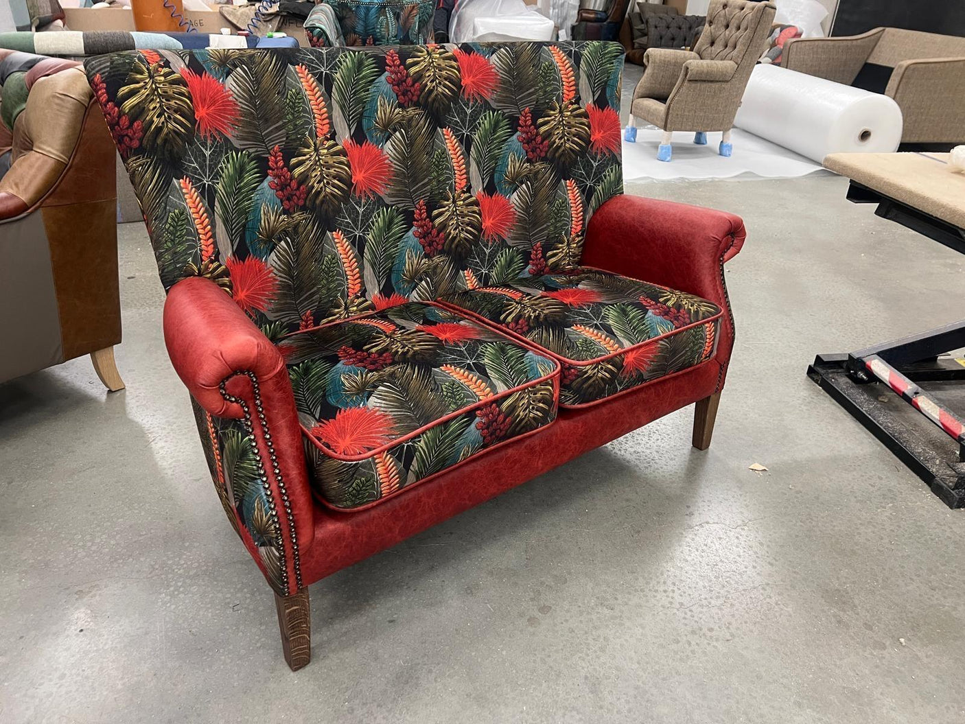 Red velvet two seater sofa with tropical palm leaf print upholstery and wooden legs