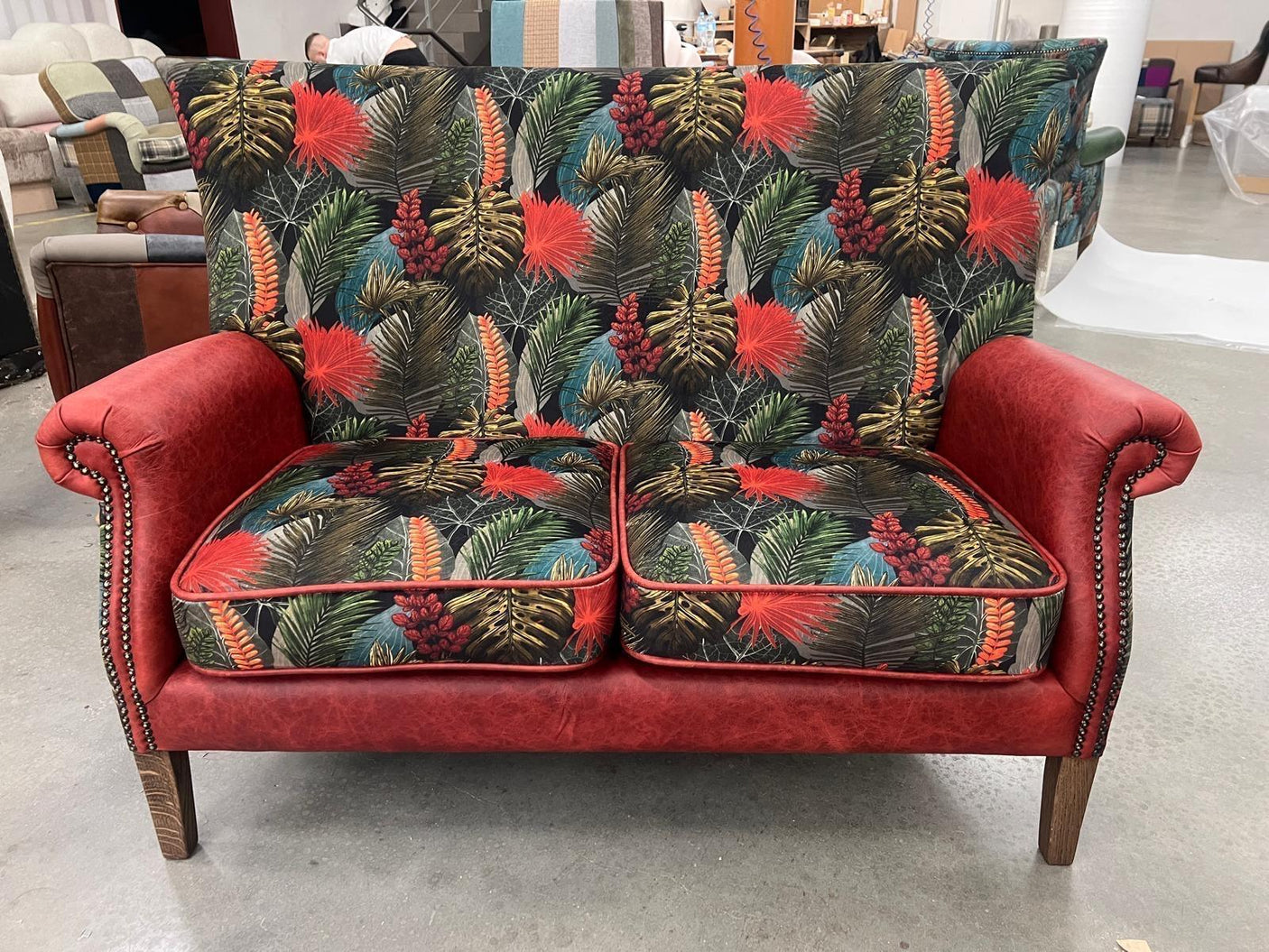 Patterned two seater sofa with red arms, nailhead trim, and tropical leaf upholstery