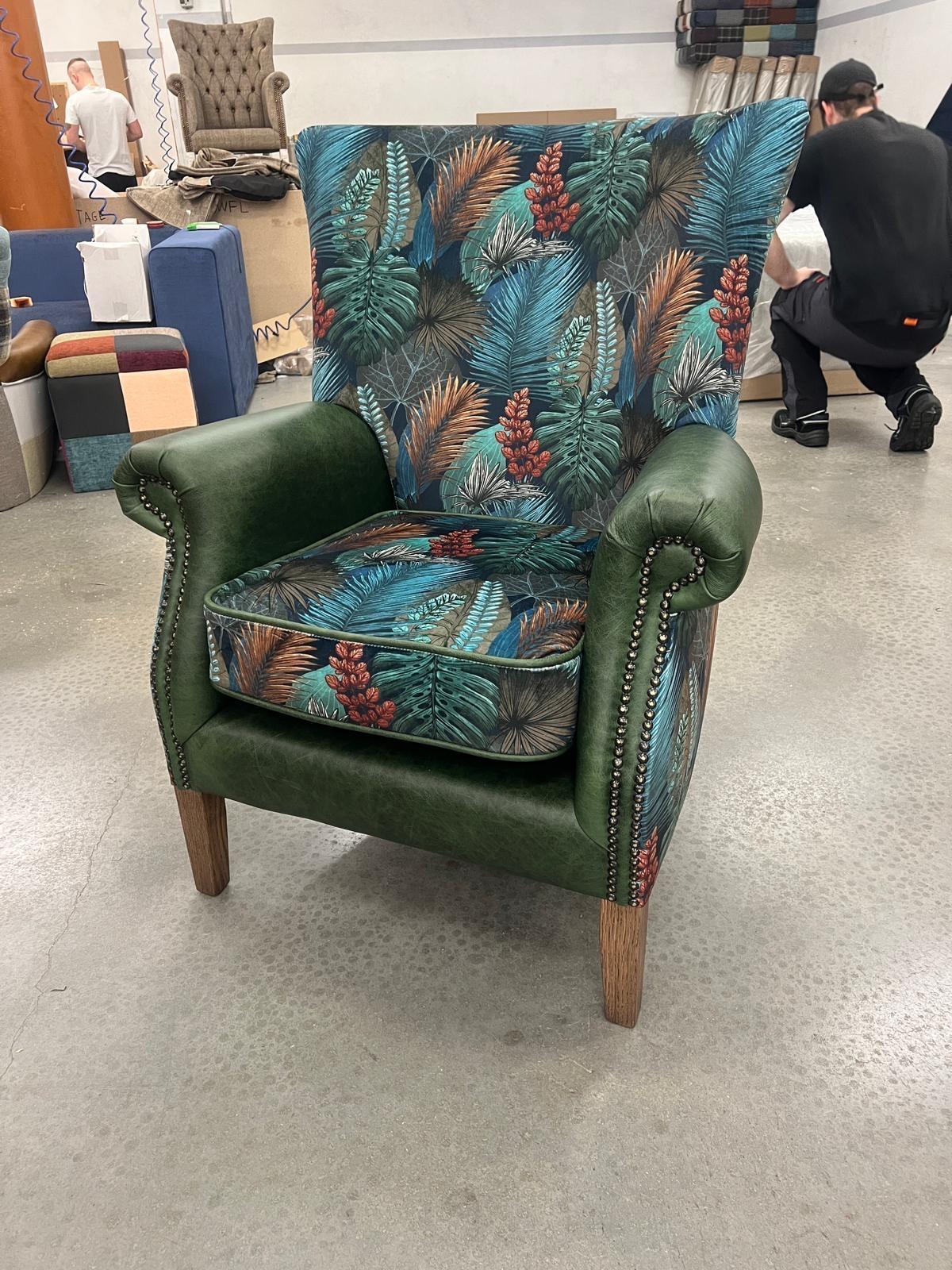 Green armchair with tropical leaf patterned upholstery and wooden legs in showroom