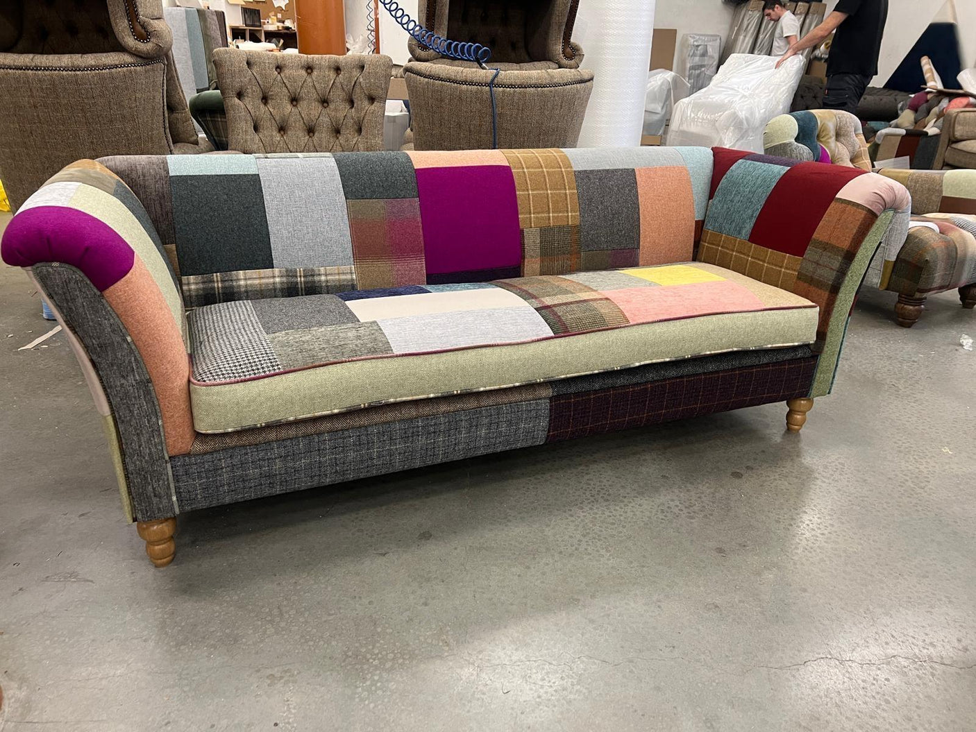 Patchwork fabric sofa with multicolor upholstery, wooden legs, and curved armrests in showroom