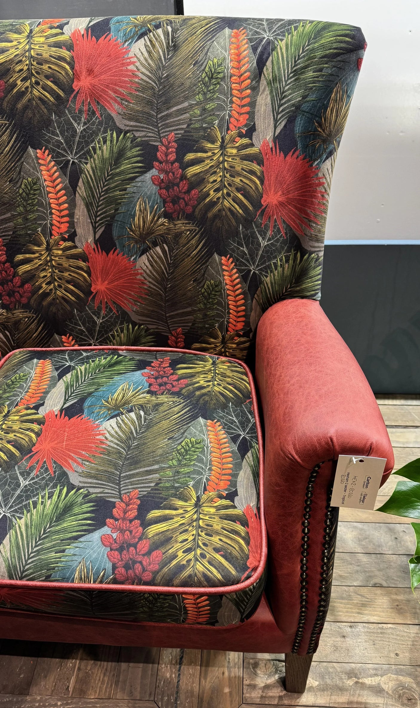 Accent armchair with tropical leaf upholstery and red faux leather armrest on wooden floor