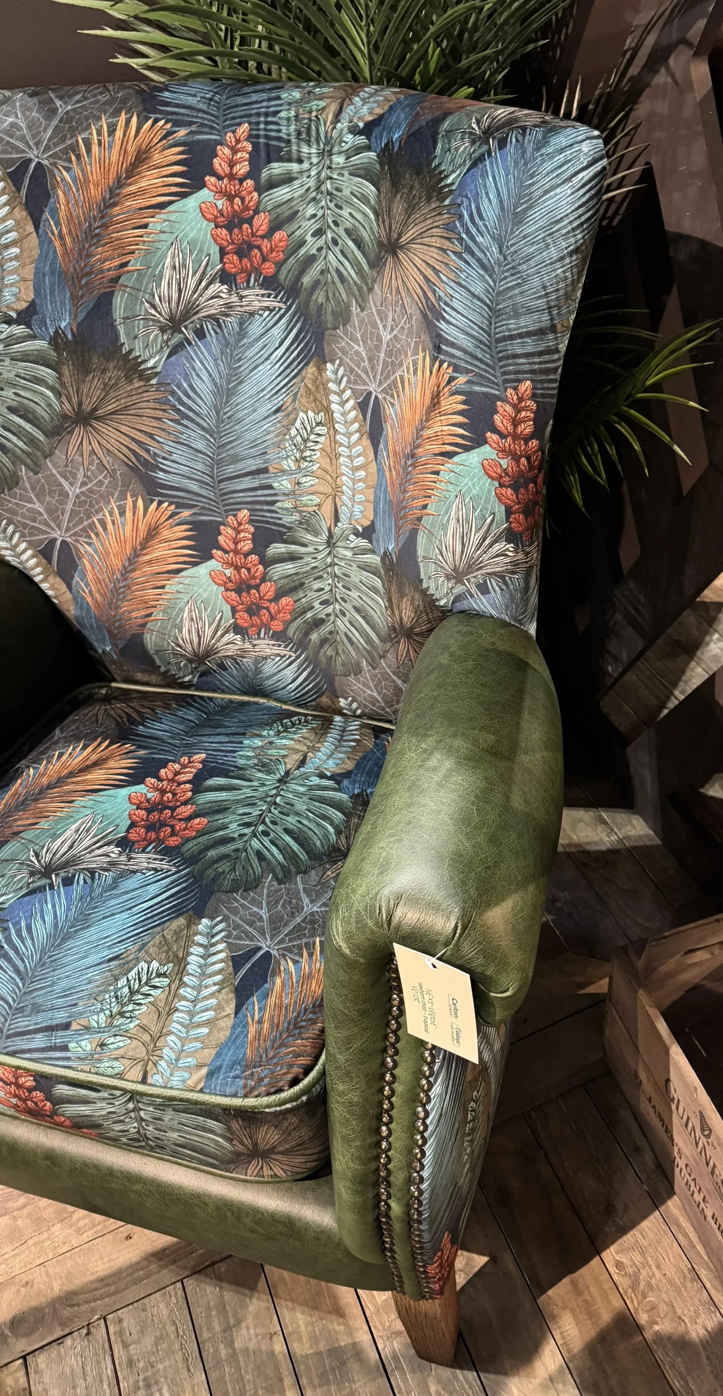 Patterned armchair with tropical leaf upholstery and green leather armrest on wooden floor
