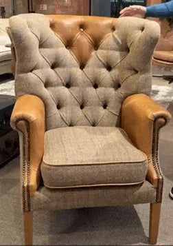 Tufted fabric armchair with tan leather arms and wooden legs in showroom setting