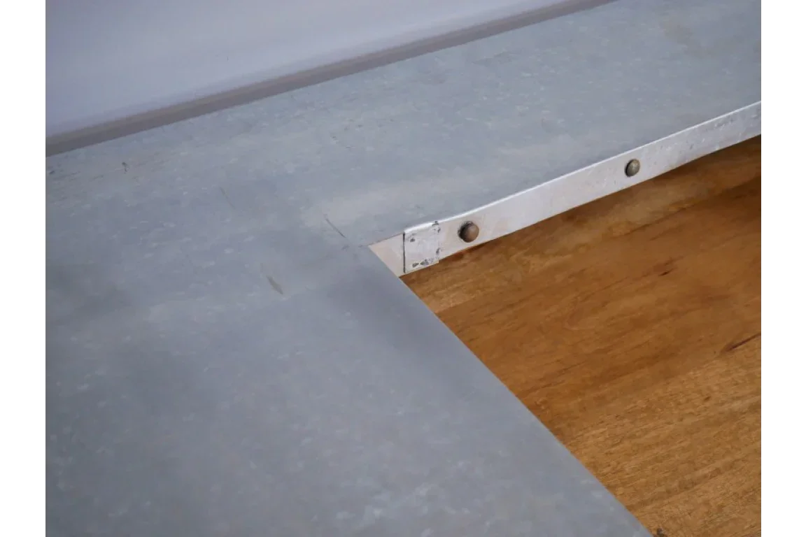 Close-up of metal dining table corner with visible rivets and wood surface underneath