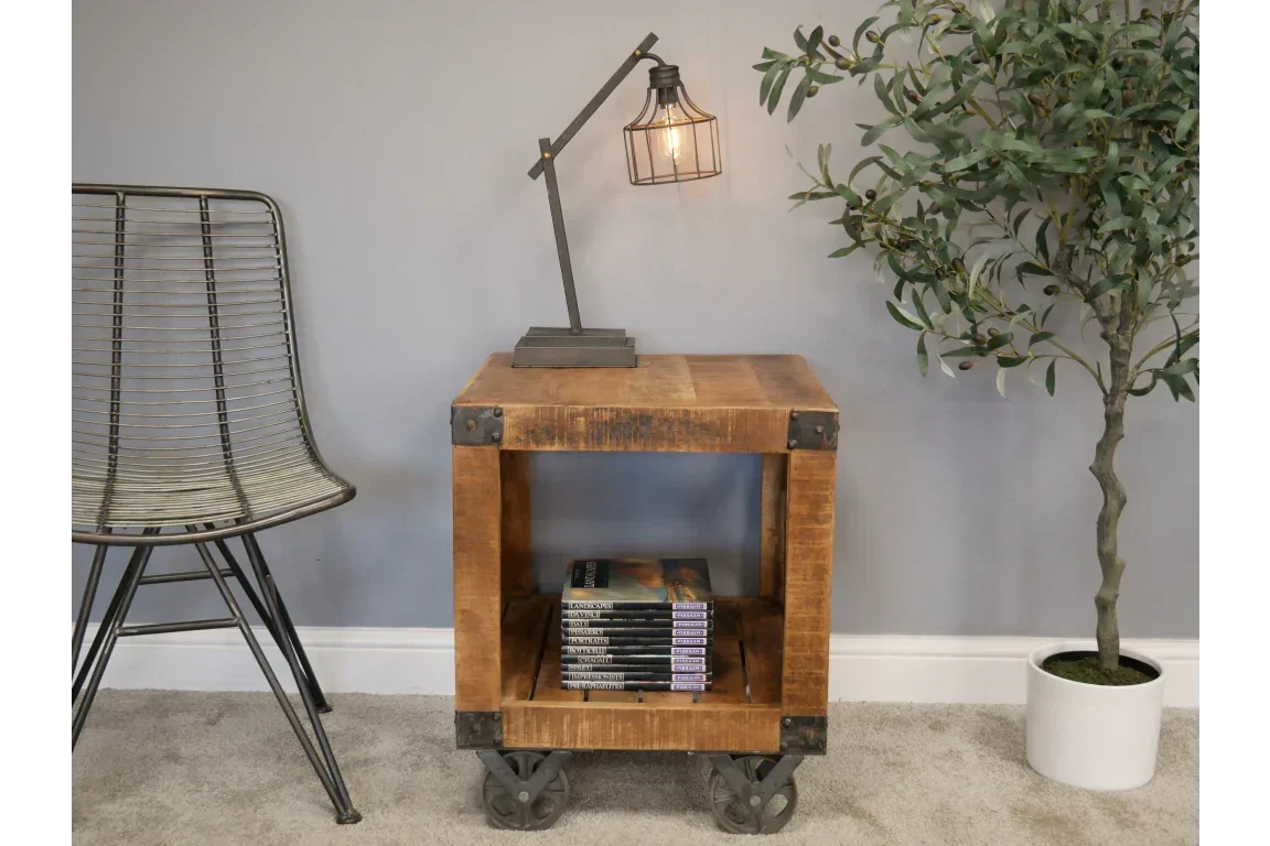 Industrial wood side table with metal accents and wheels, lamp and books displayed on carpet