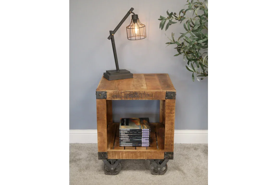 Industrial wood side table with metal wheels, lower shelf holding books, table lamp on top