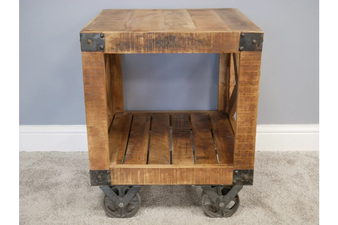 Industrial wood side table with open shelf and metal wheels on carpet floor