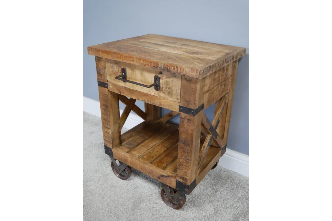 Rustic wooden side table with metal wheels, single drawer and lower shelf on carpeted floor