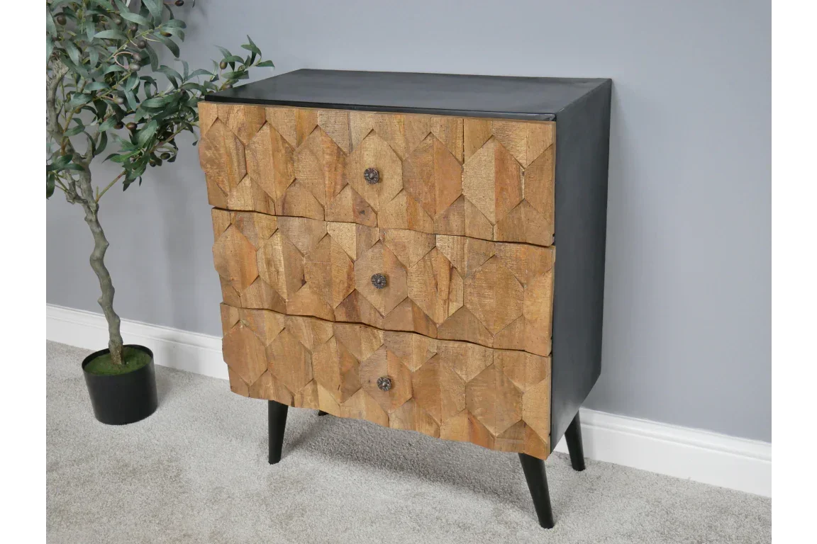 Wooden chest of drawers with geometric carved front and black legs against grey wall