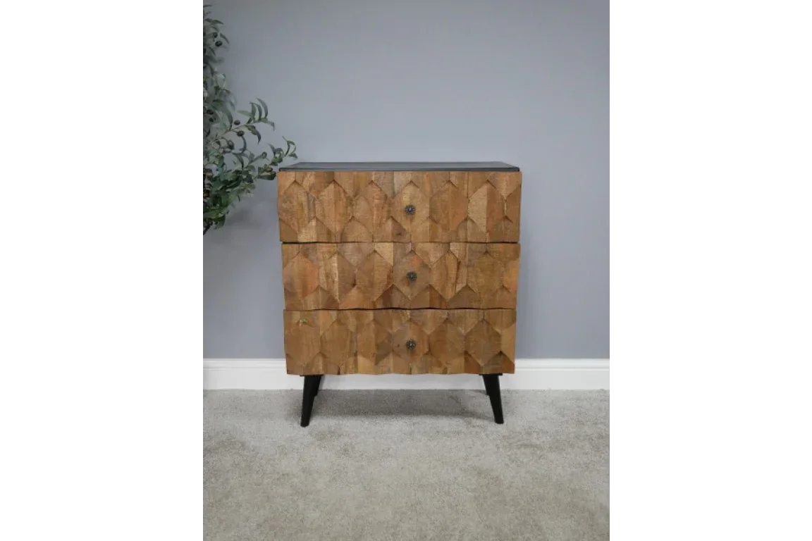 Three drawer wooden chest with geometric carved front and angled black legs on grey carpet