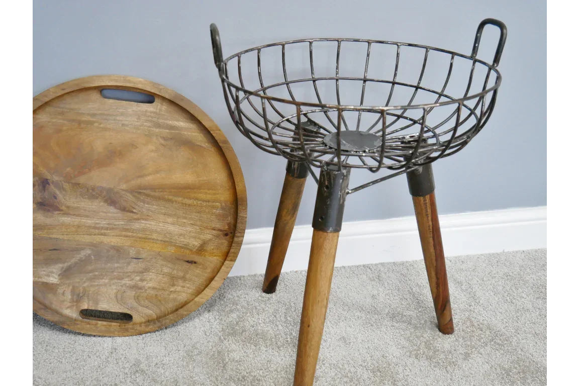 Round wooden tray beside a metal wire basket side table with wooden legs on carpet