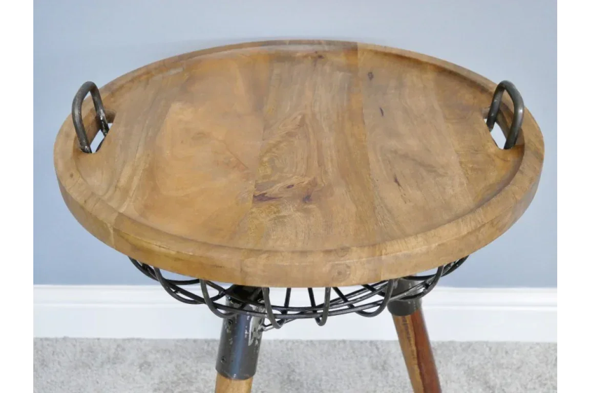 Round wooden side table with metal handles and tripod legs against blue wall