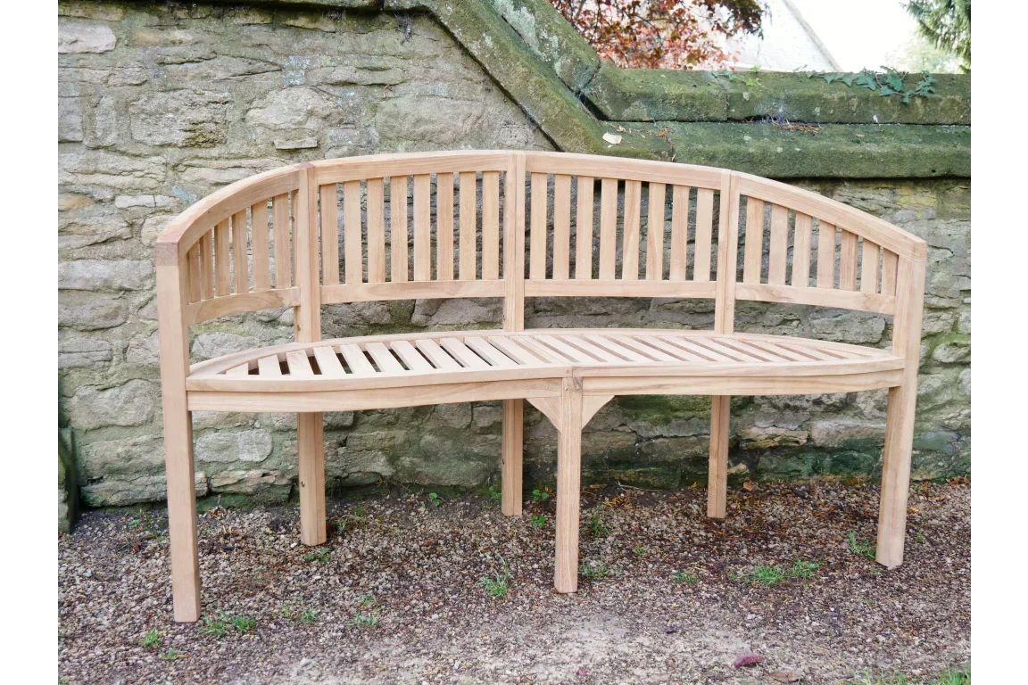 Curved wooden garden bench with slatted seat and backrest set against stone wall