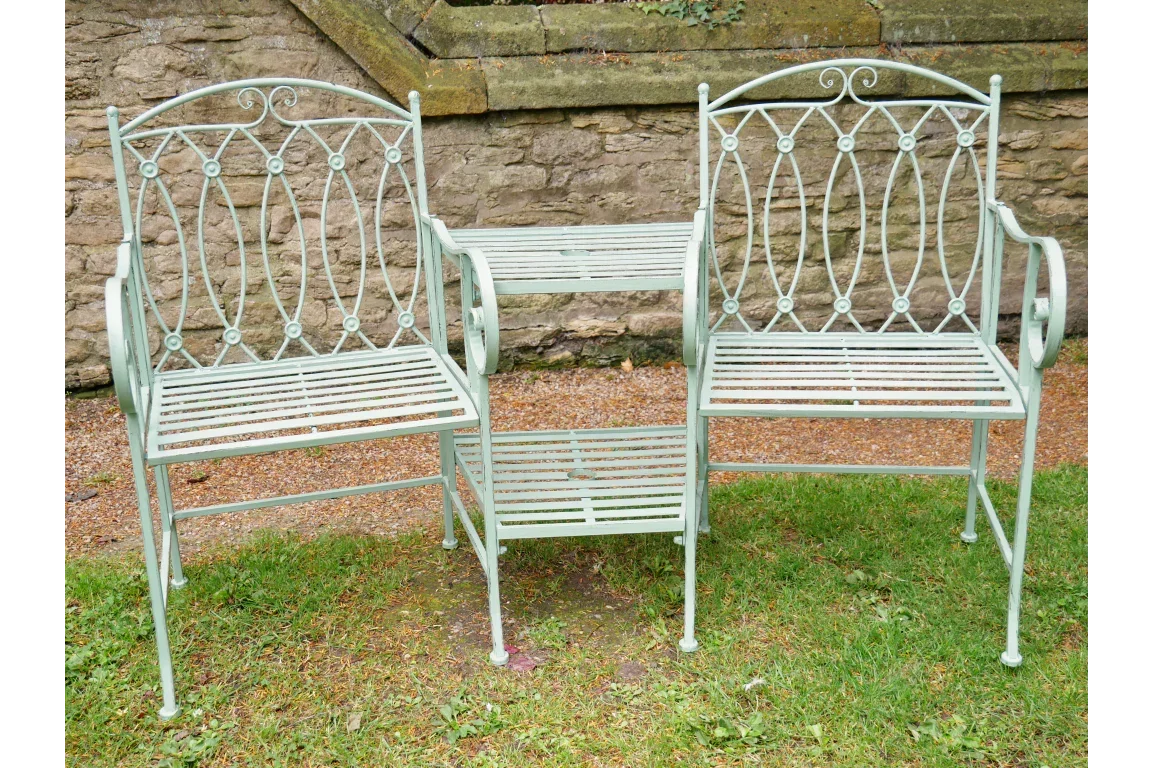 Green metal garden bench set with two chairs and side table on grass