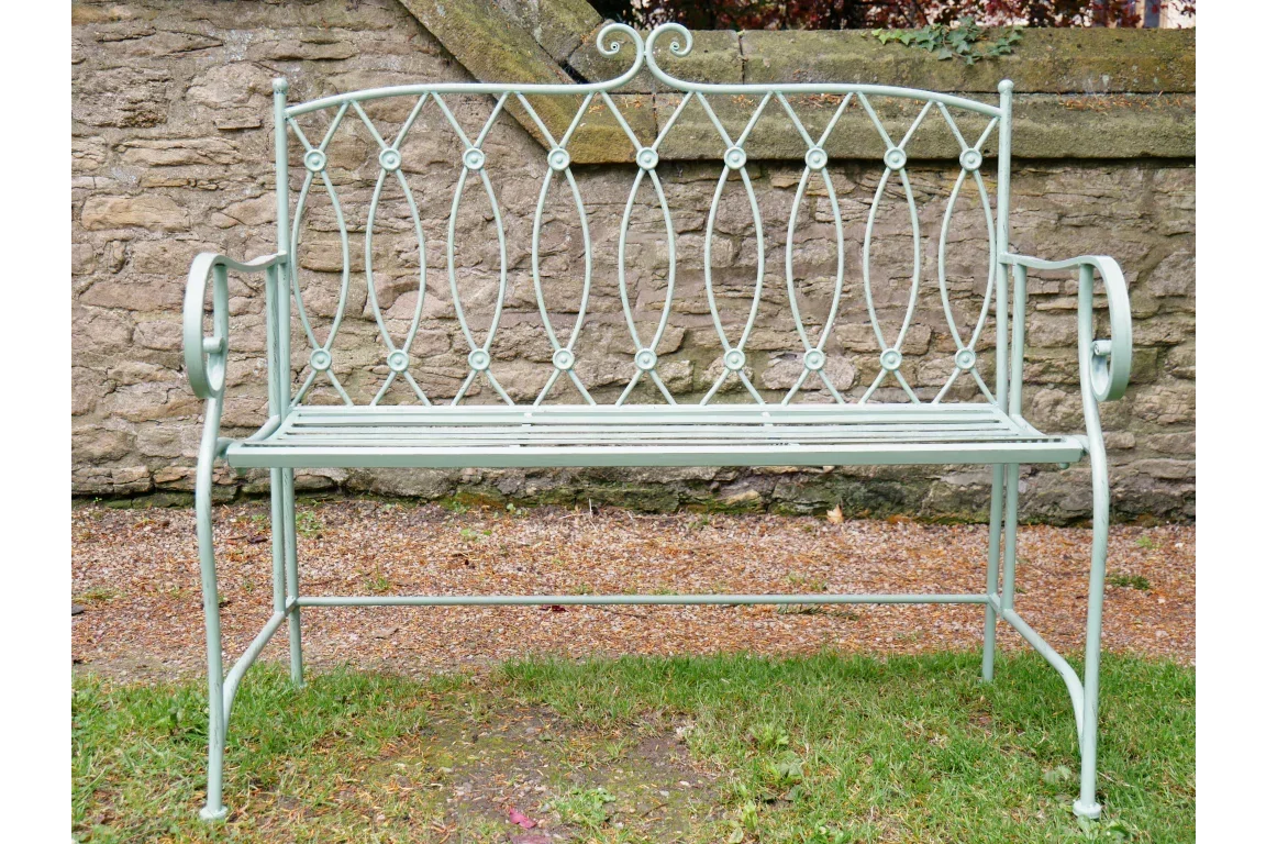 Light green metal garden bench with ornate scrollwork backrest on grass