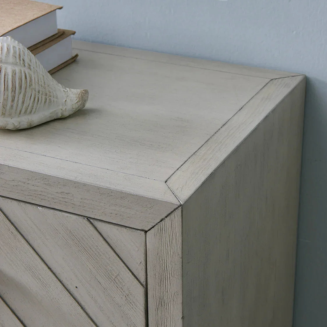 Light wood sideboard corner with chevron detail, decorative shell, and books on top