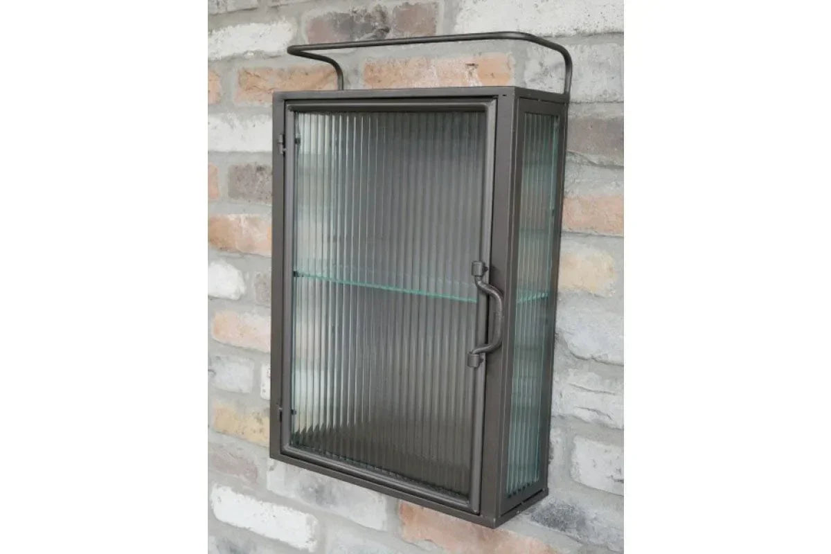 Wall mounted metal display cabinet with ribbed glass door and shelf against brick wall