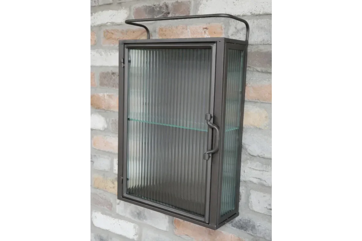 Black metal wall cabinet with ribbed glass door and interior shelf mounted on brick wall