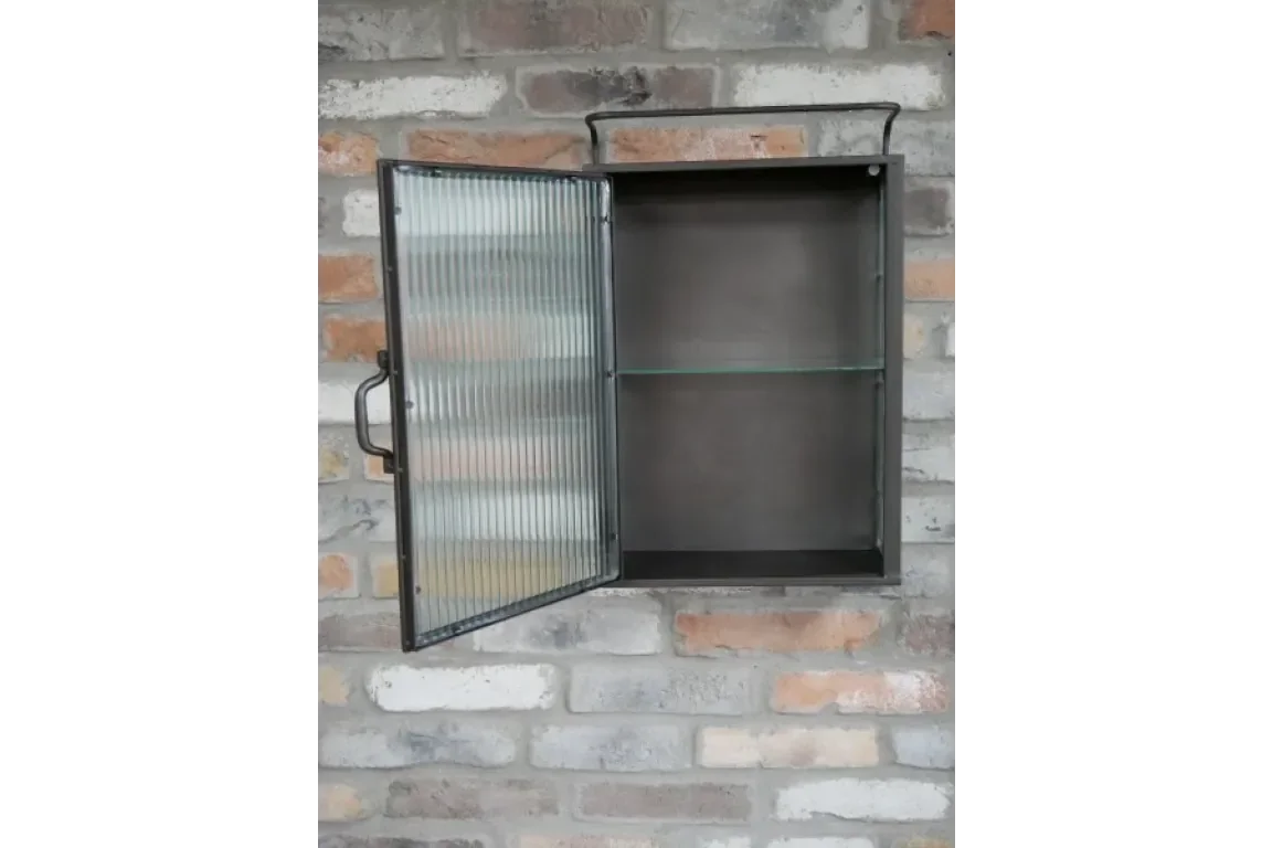 Black metal wall cabinet with ribbed glass door and shelf, open against brick wall
