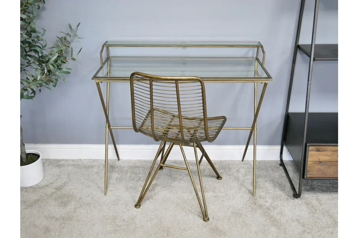 Glass writing desk with gold metal frame and matching gold wire chair on grey carpet