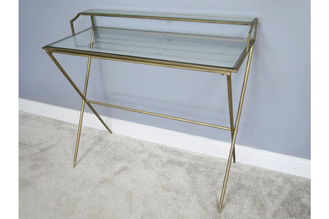Glass console table with slim gold metal frame against light grey wall on carpeted floor