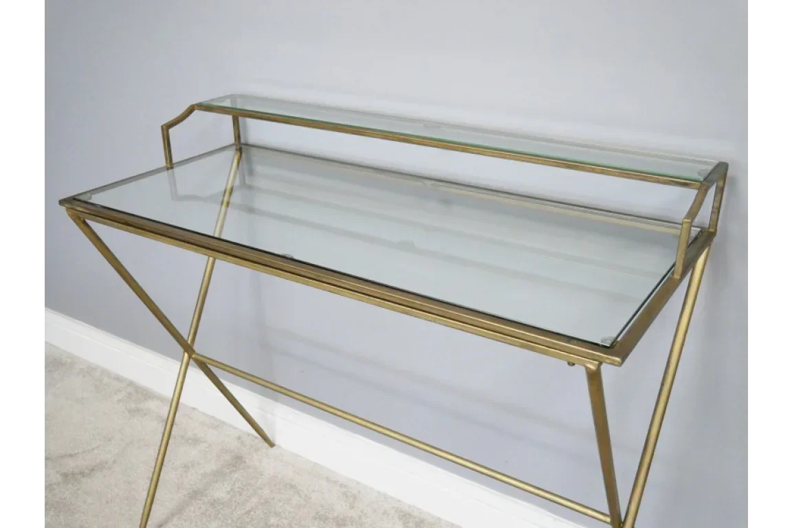 Glass console table with gold metal frame and raised shelf against grey wall