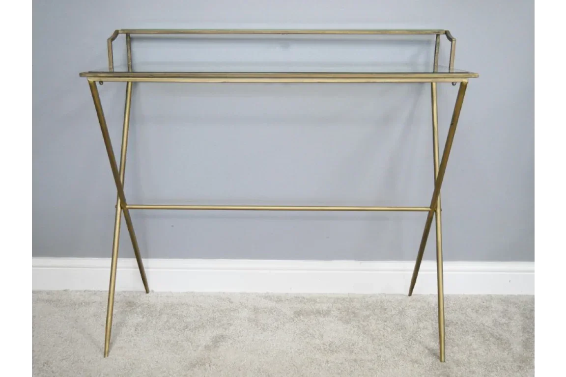 Gold metal console table with clear glass shelf against light grey wall on carpeted floor