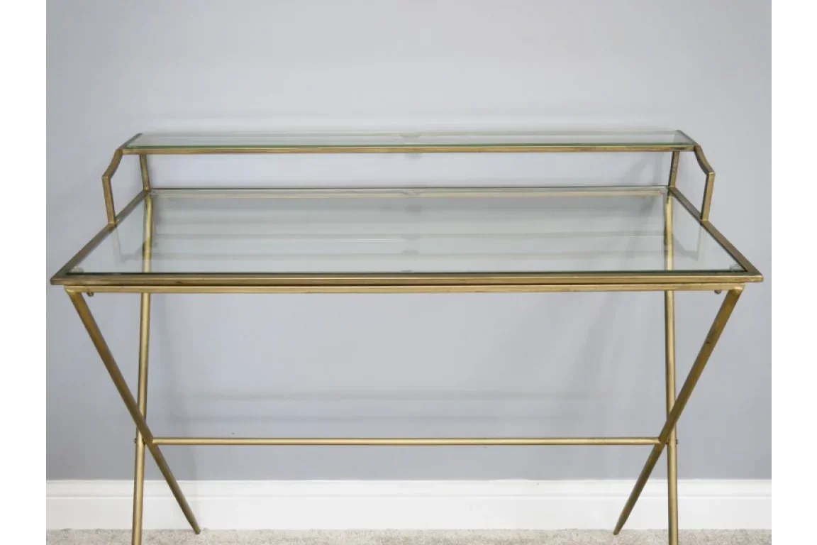 Glass top console table with gold metal frame and raised shelf against grey wall