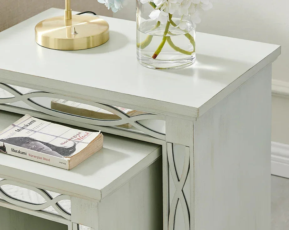 White mirrored bedside table with floral vase, lamp, and book on top surface
