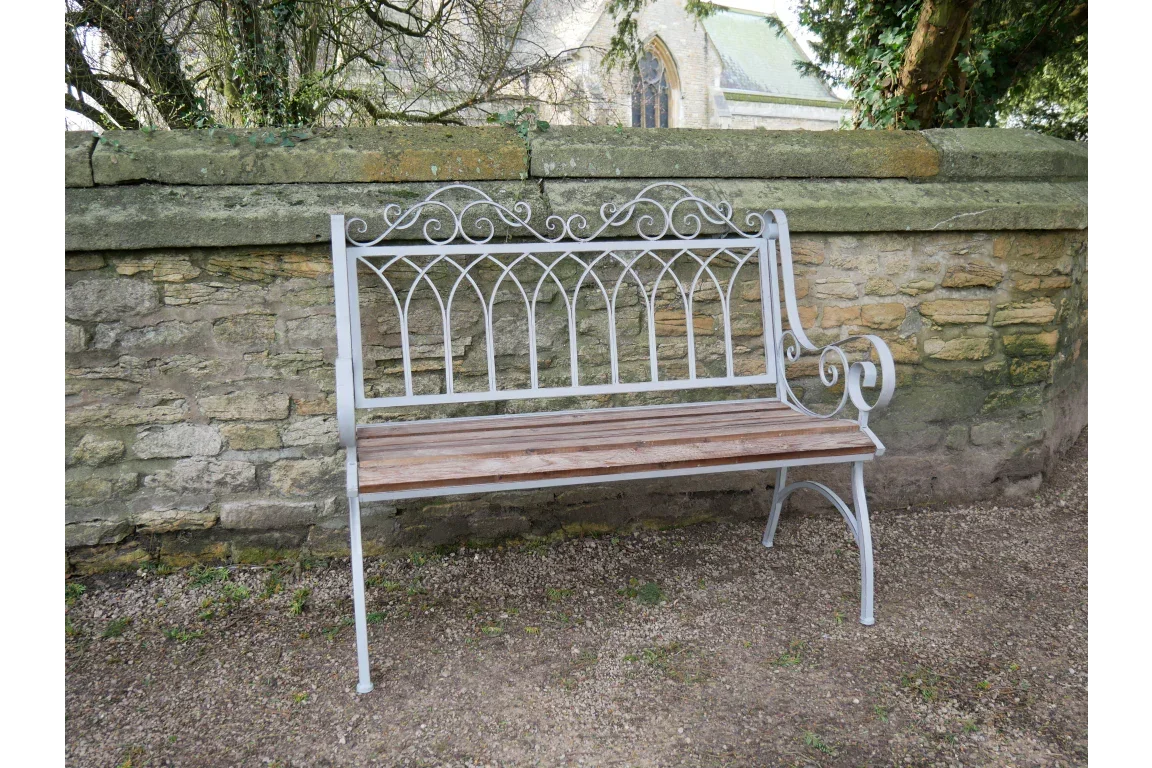 Metal garden bench with decorative back and wooden seat set against stone wall outdoors