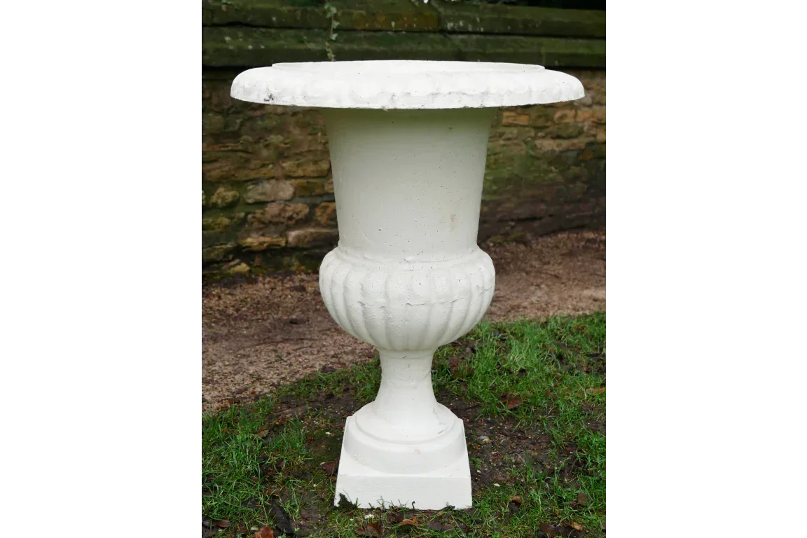 White stone garden planter urn with fluted base on lawn beside stone wall