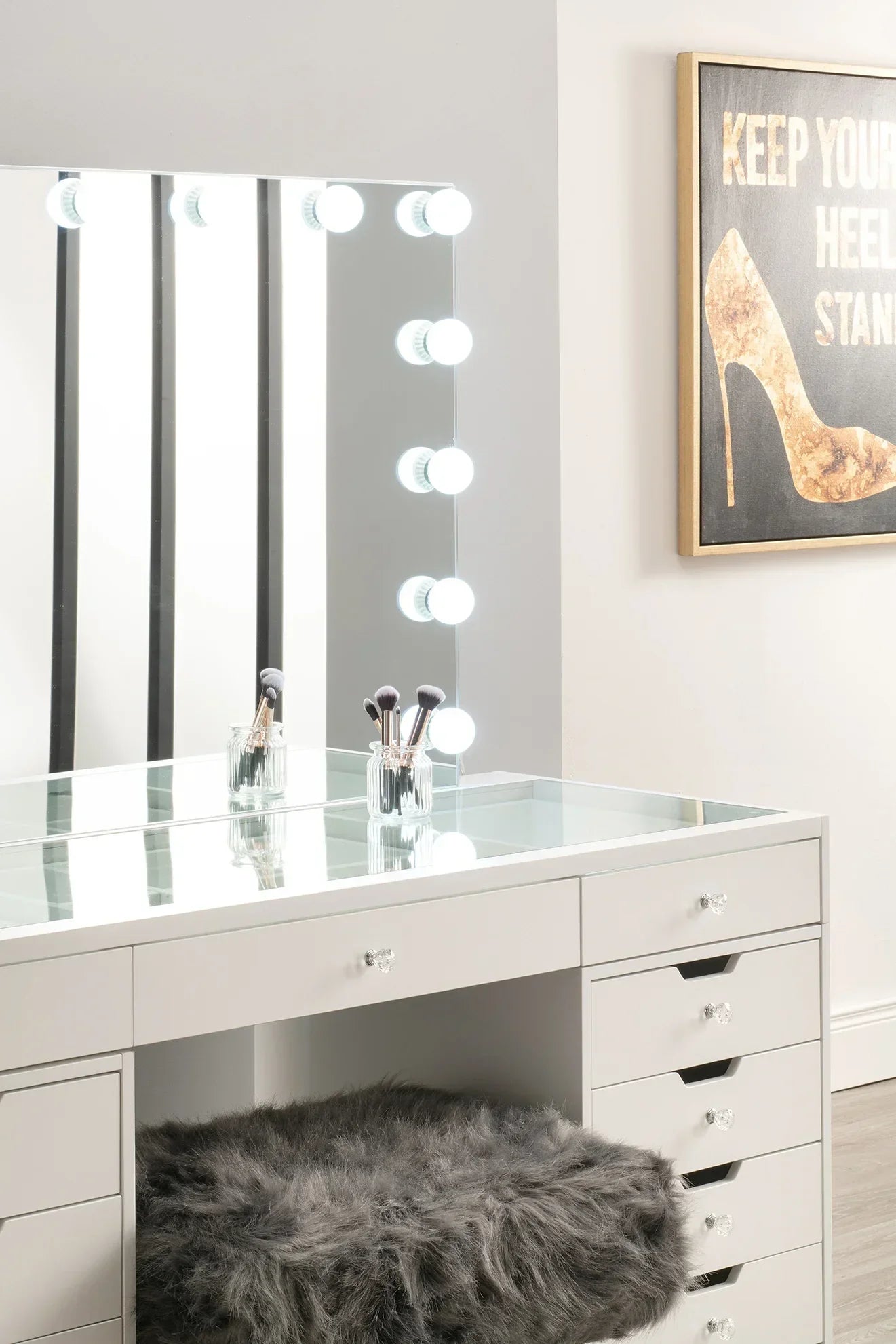 White dressing table with Hollywood mirror, fur stool, and makeup brushes in glass jar