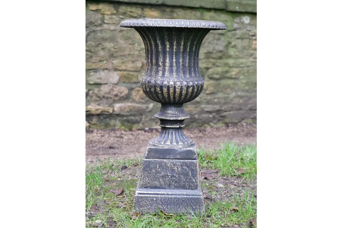 Black cast iron garden urn planter with fluted design on stone base outdoors