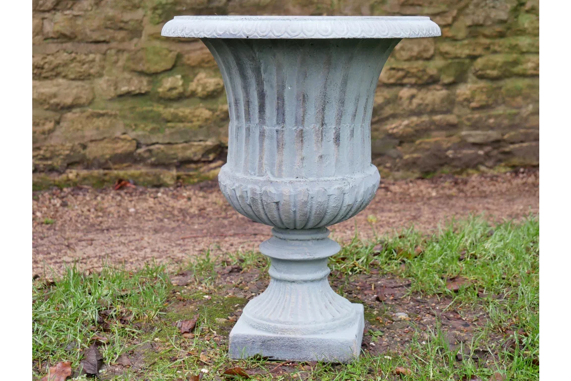 Grey stone effect garden urn planter on grass next to a stone wall