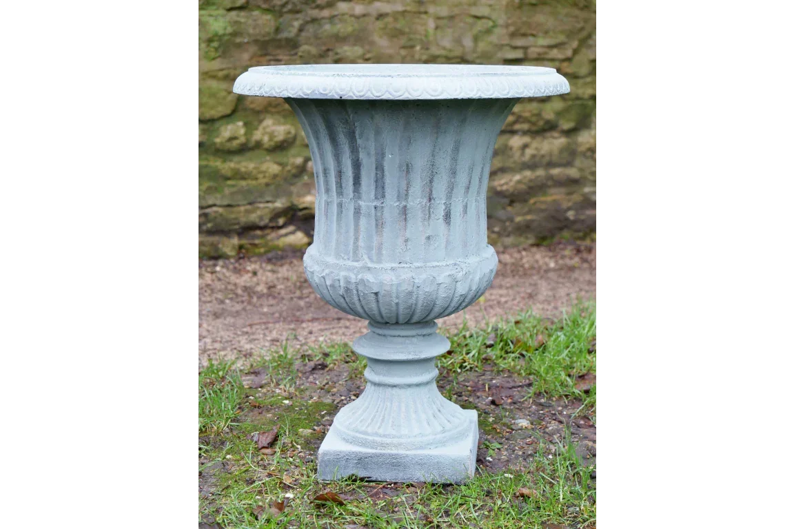 Grey stone garden planter urn with fluted design on grass near a stone wall