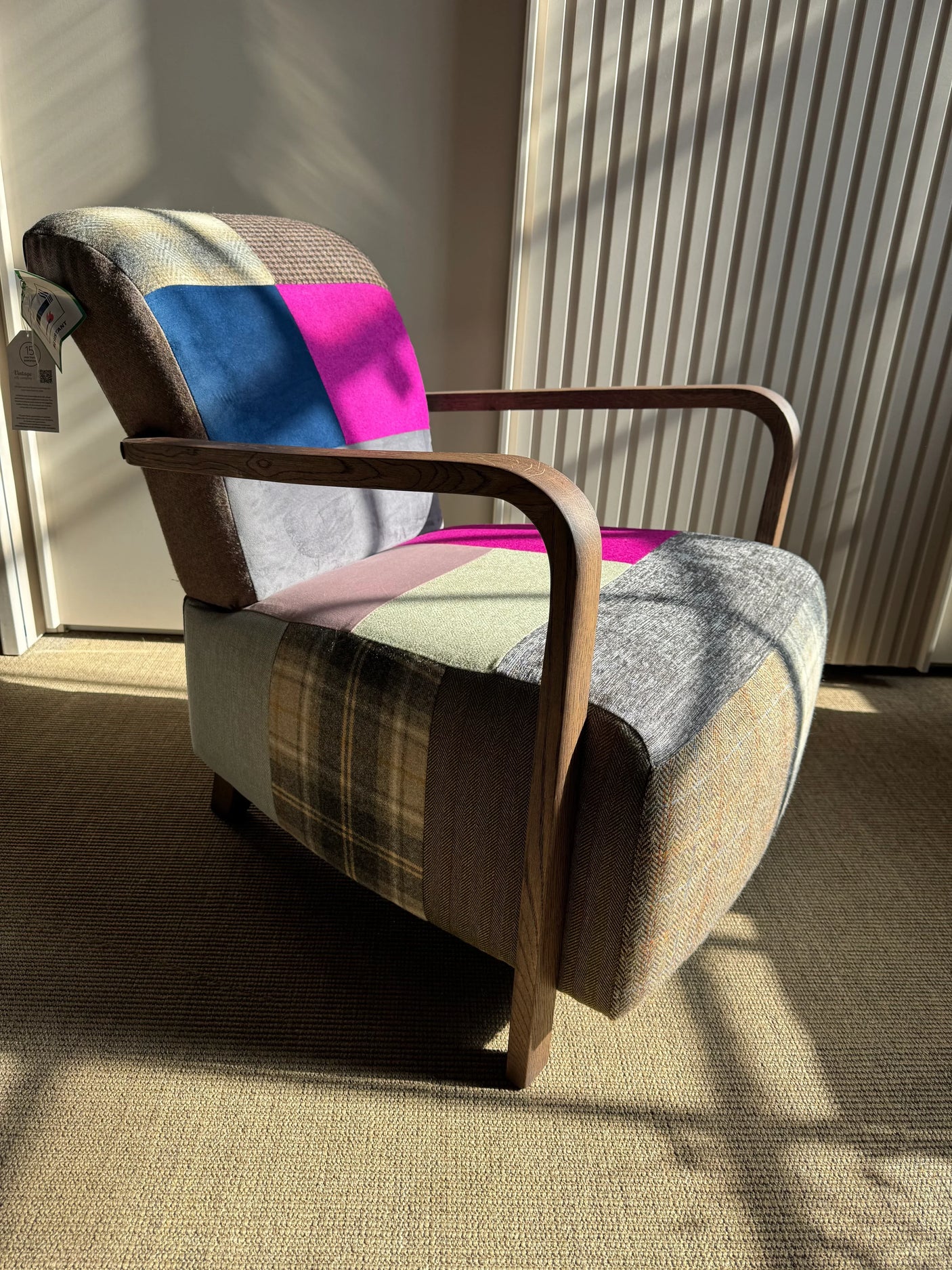 Patchwork accent chair with wooden arms and multicoloured fabric upholstery in sunlight