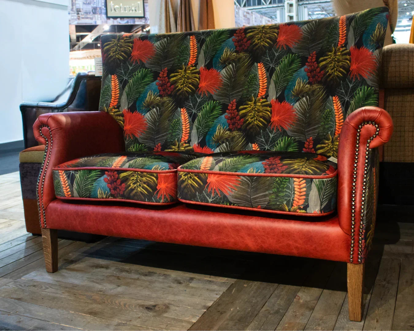 Red leather sofa with tropical leaf upholstery and wooden legs on showroom floor
