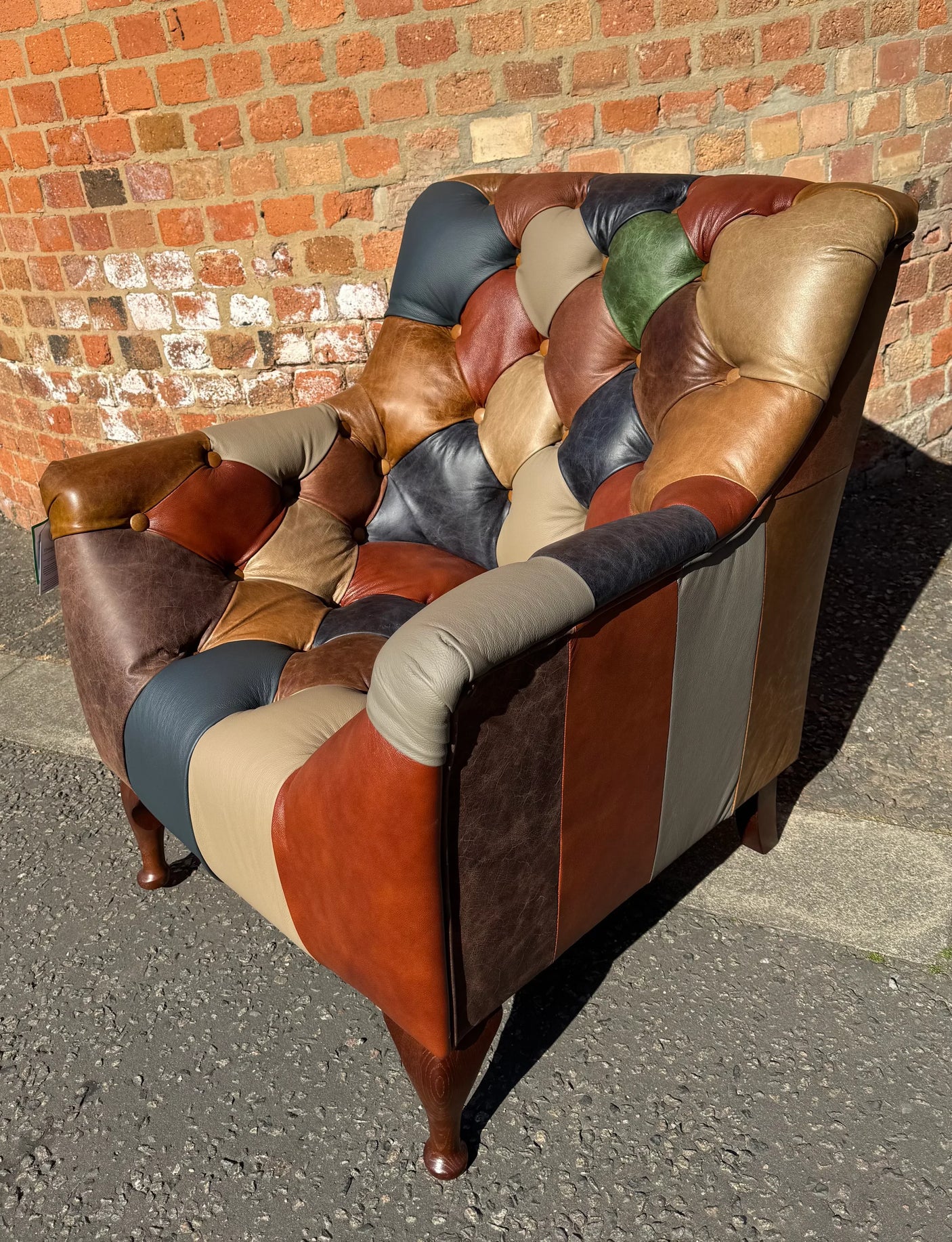 Patchwork leather armchair with button-tufted backrest against brick wall outdoors