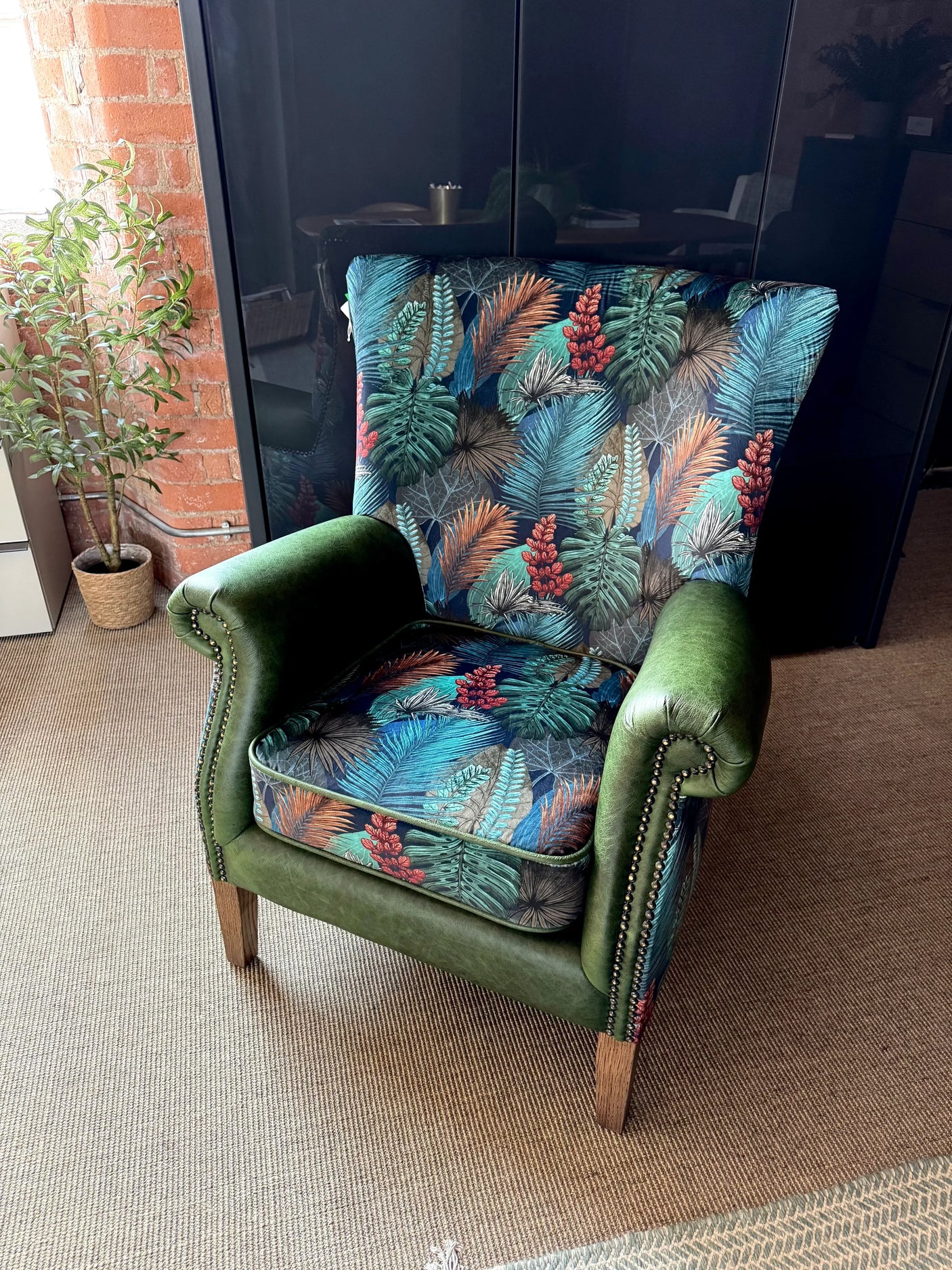 Green velvet armchair with tropical leaf patterned upholstery and wooden legs
