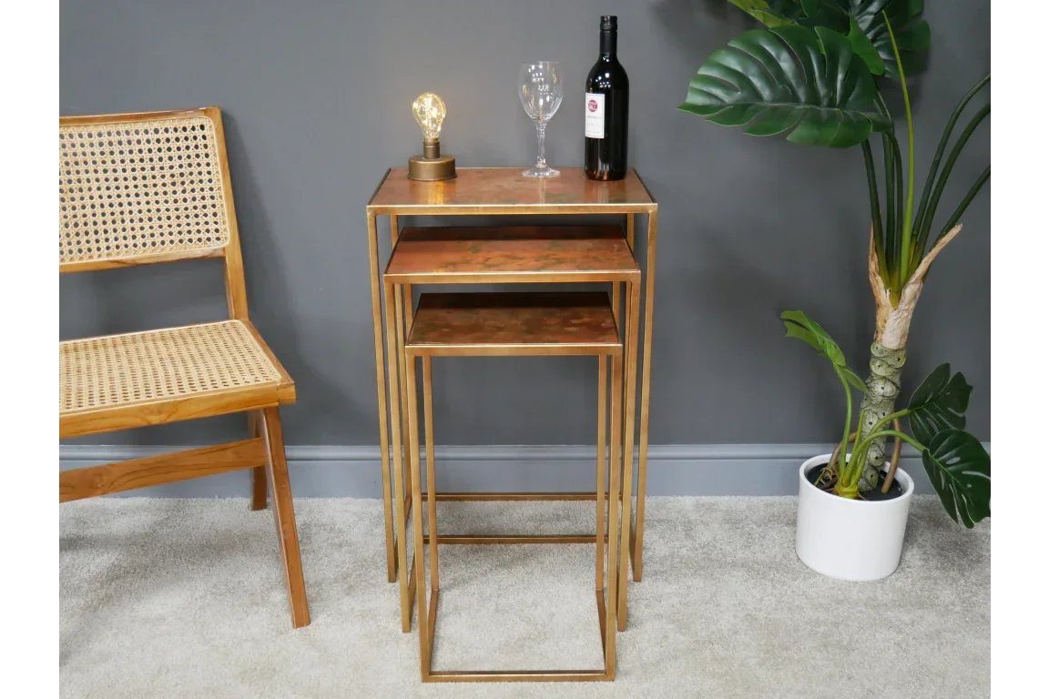 Set of three gold nesting tables beside cane chair and potted plant in living room