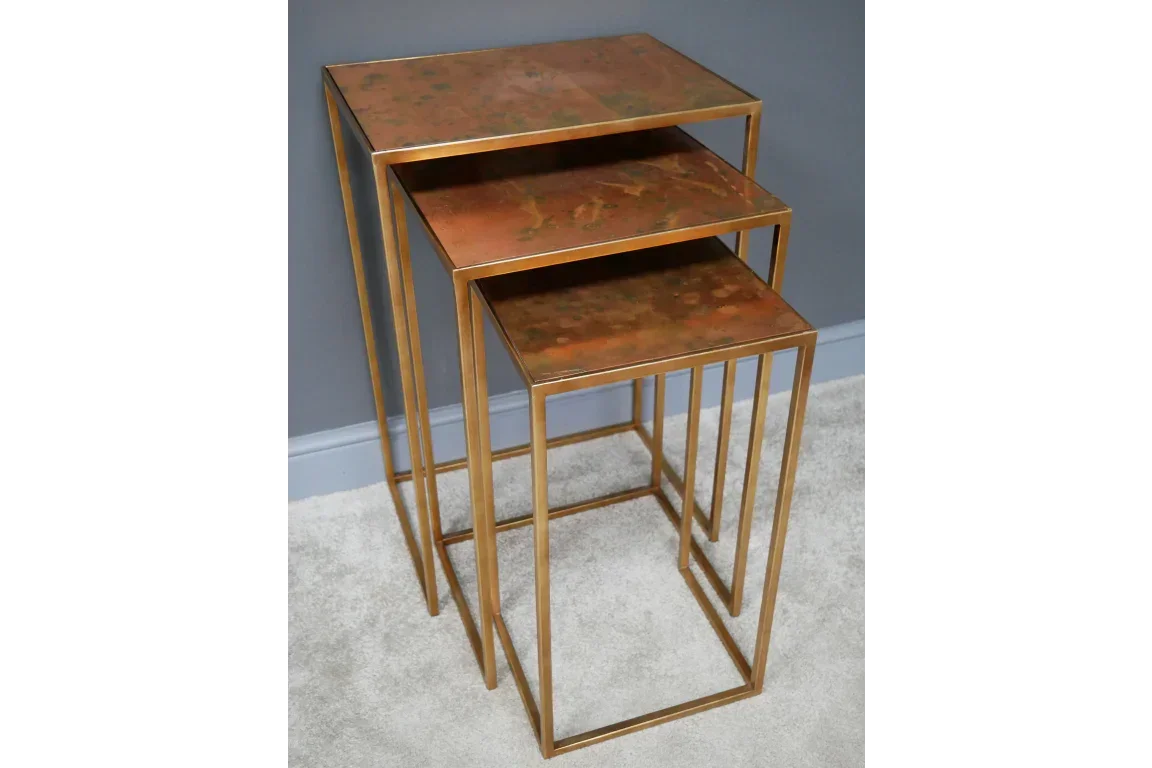 Set of three metal nesting tables with bronze tops and gold frames on grey carpet