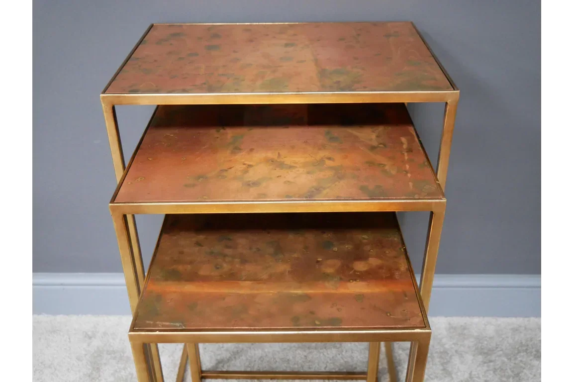 Set of three gold metal nesting tables with distressed copper tops against grey wall