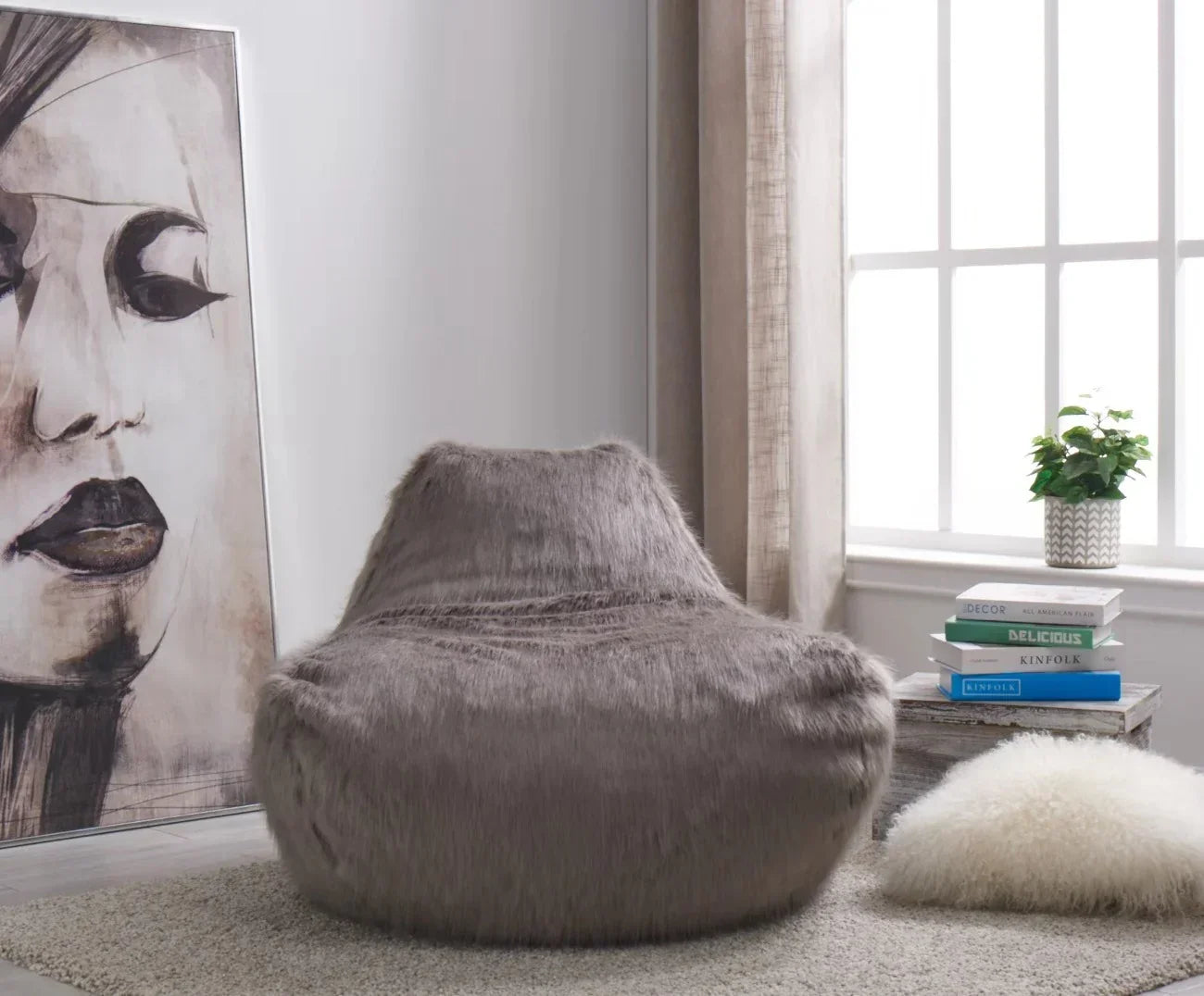 Grey faux fur bean bag chair in modern living room with books and potted plant by window