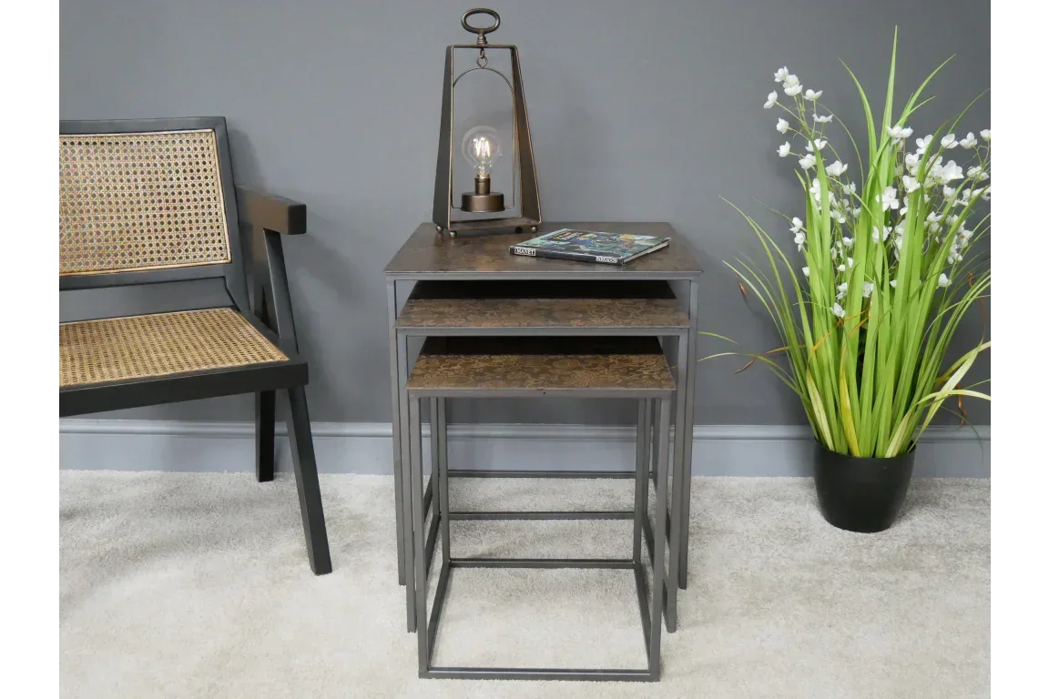 Nest of tables with metal legs and wood tops beside woven chair and artificial plant